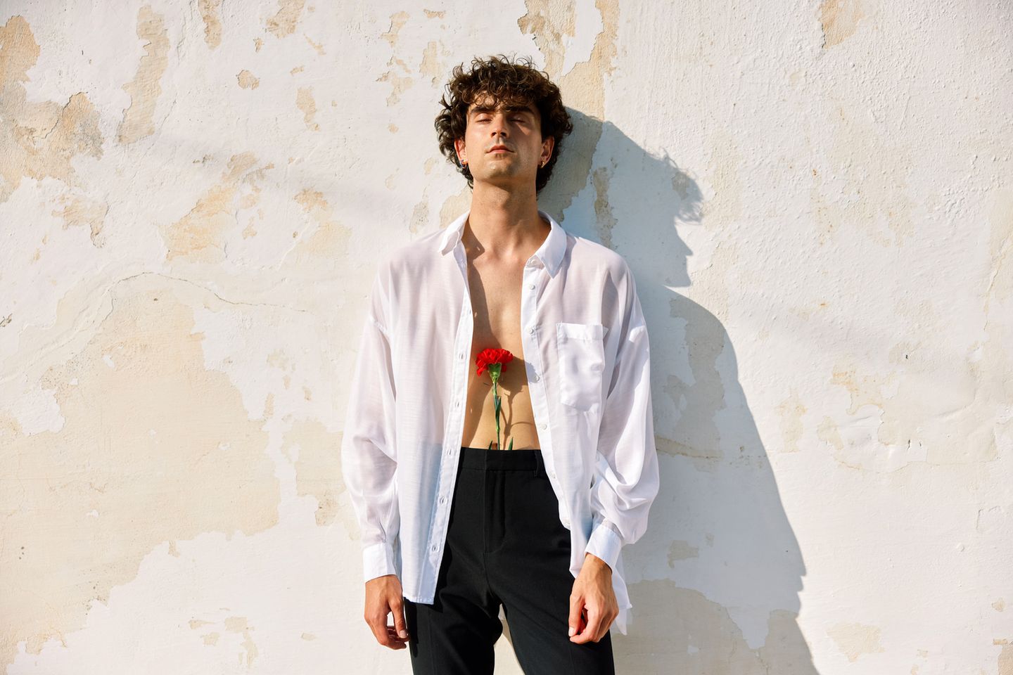 ein Mann lehnt an einer Mauer mit einer Rose in der Hose