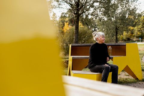 Eine ältere Frau sitzt auf einer Bank in einem Park