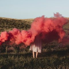 Eine Frau steht auf einer Wiese in roten Rauch gehüllt