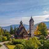 Holzkirche mit spitzen Türmen, daneben hoher Turm, im Hintergrund Berge, herbstliche Stimmiung