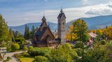 Holzkirche mit spitzen Türmen, daneben hoher Turm, im Hintergrund Berge, herbstliche Stimmiung