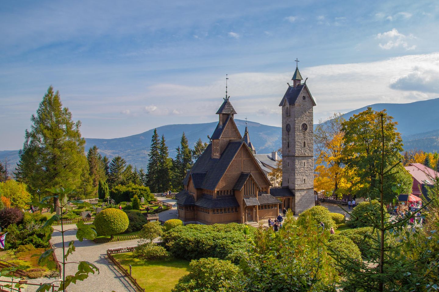 Holzkirche mit spitzen Türmen, daneben hoher Turm, im Hintergrund Berge, herbstliche Stimmiung