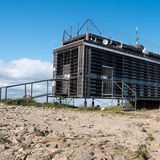 Kistenartiges Holz auf Stelzen mit Satellitenschüsseln, davor Geröll