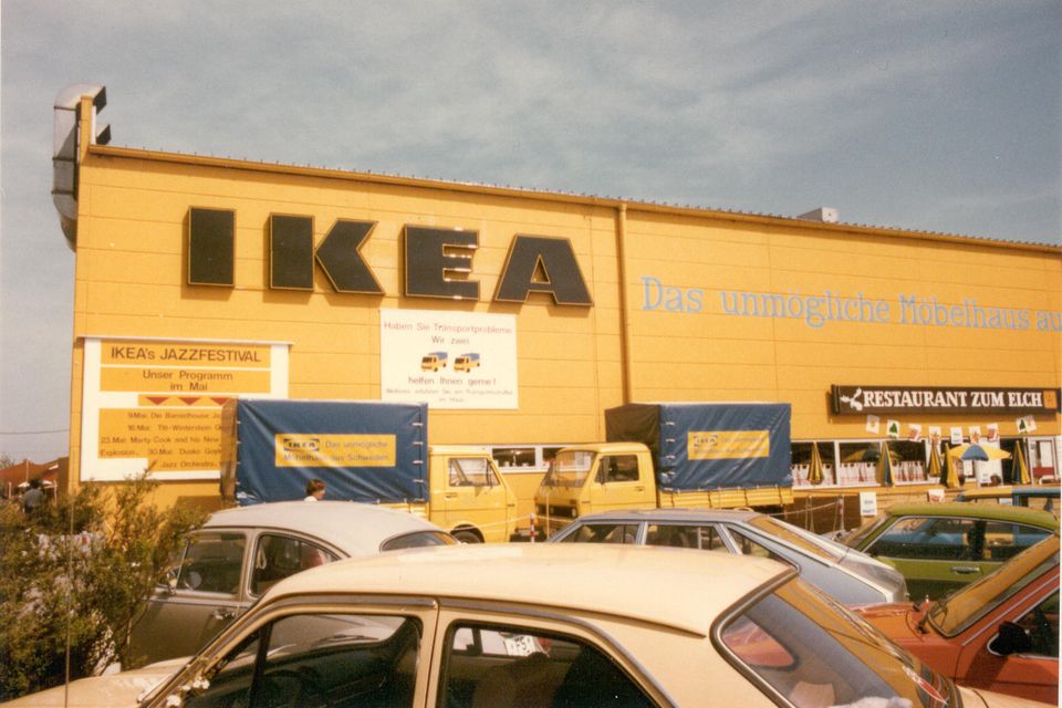 Gelbe Fassade eines Ikea-Möbelhauses, davor zwei Lieferwagen und parkende Autos
