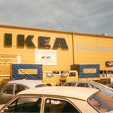 Gelbe Fassade eines Ikea-Möbelhauses, davor zwei Lieferwagen und parkende Autos