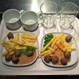 Tablett, darauf zwei Teller mit Hackbällchen, Pommes, Erbsen sowie Becher und Gläser