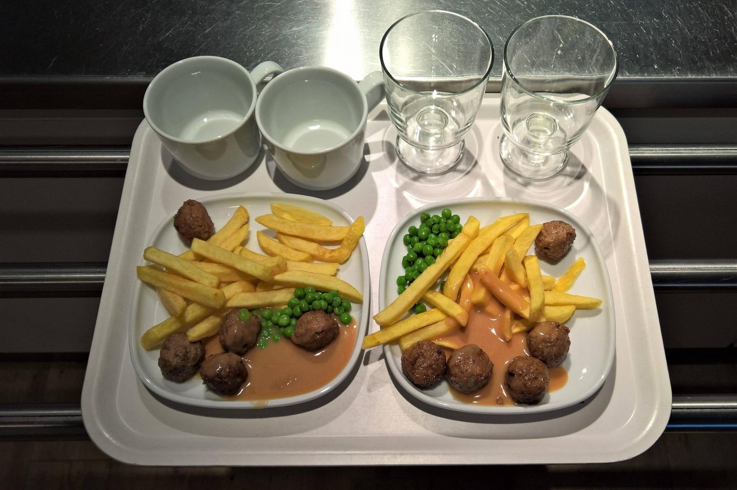 Wer satt ist, kauft mehr Tablett, darauf zwei Teller mit Hackbällchen, Pommes, Erbsen sowie Becher und Gläser