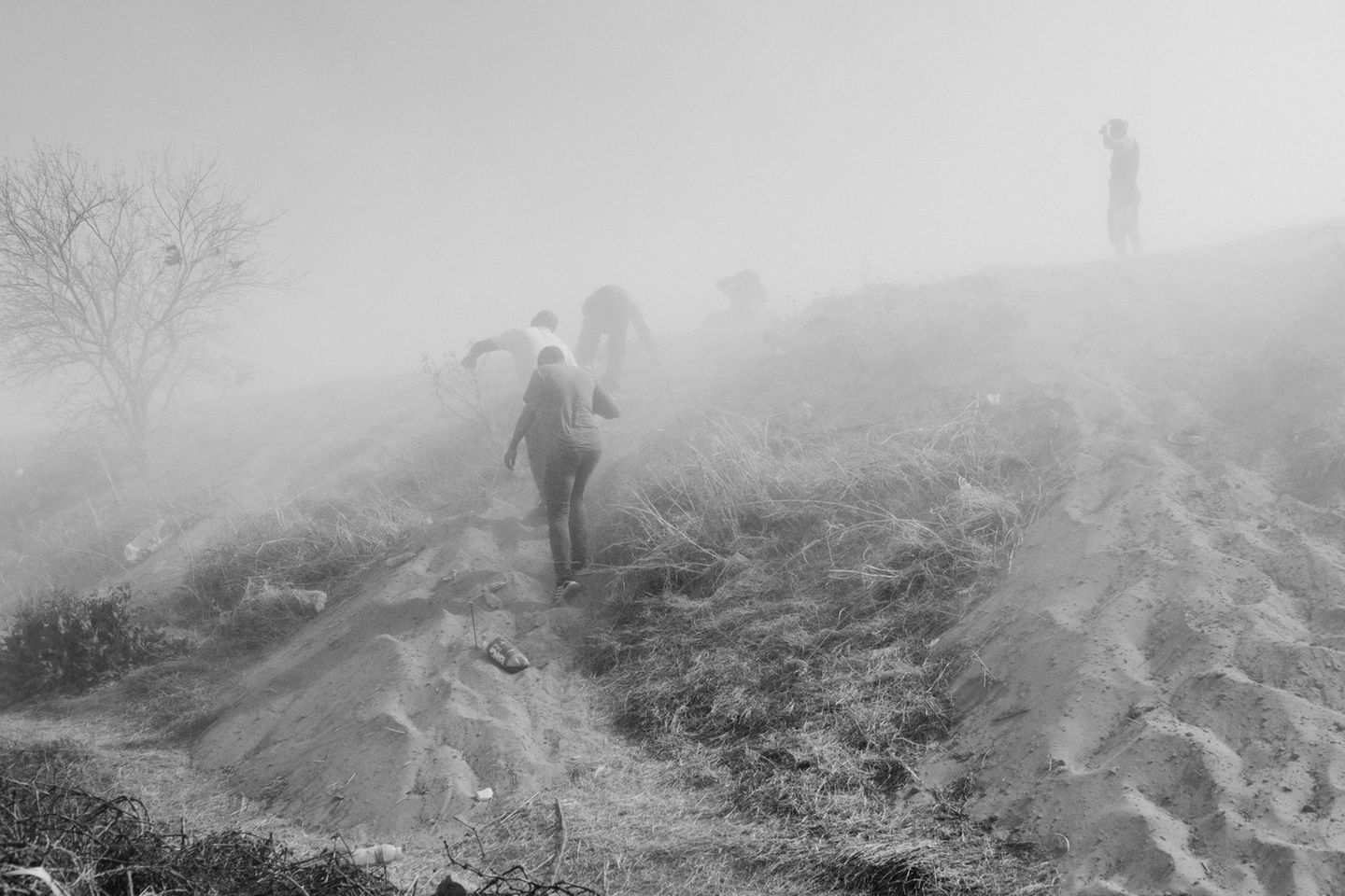 Schwarz-weiß Fotografie: Menschen laufen durch Nebel einen Hügel hinauf