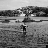 Schwarz-weiß Fotografie: Ein Mann trägt eine alte Frau durch einen Fluss