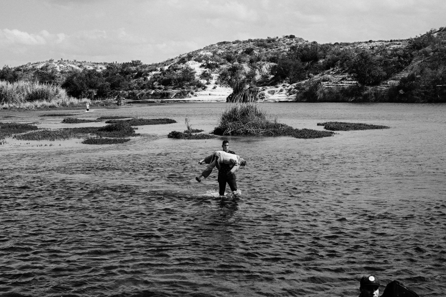 Schwarz-weiß Fotografie: Ein Mann trägt eine alte Frau durch einen Fluss