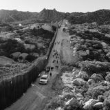 Schwarz-weiß Fotografie: Männer laufen auf einer verlassenen Straße einem weißen Auto hinterher