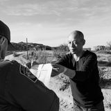 Schwarz-weiß Fotografie: Ein Mann wird von einem US-Grenzpolizisten kontrolliert