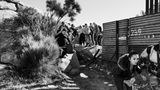 Schwarz-weiß Fotografie: Asylsuchende laufen durch eine Lücke im Grenzzaun zwischen Mexiko und USA