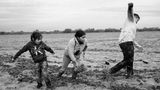 Schwarz-weiß Fotografie: Mutter und zwei Kinder laufen angestrengt durch tiefen Schlamm