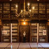 Holzregale voller Bücher über zwei Etagen mit Galerie, in der Mitte eine Büste