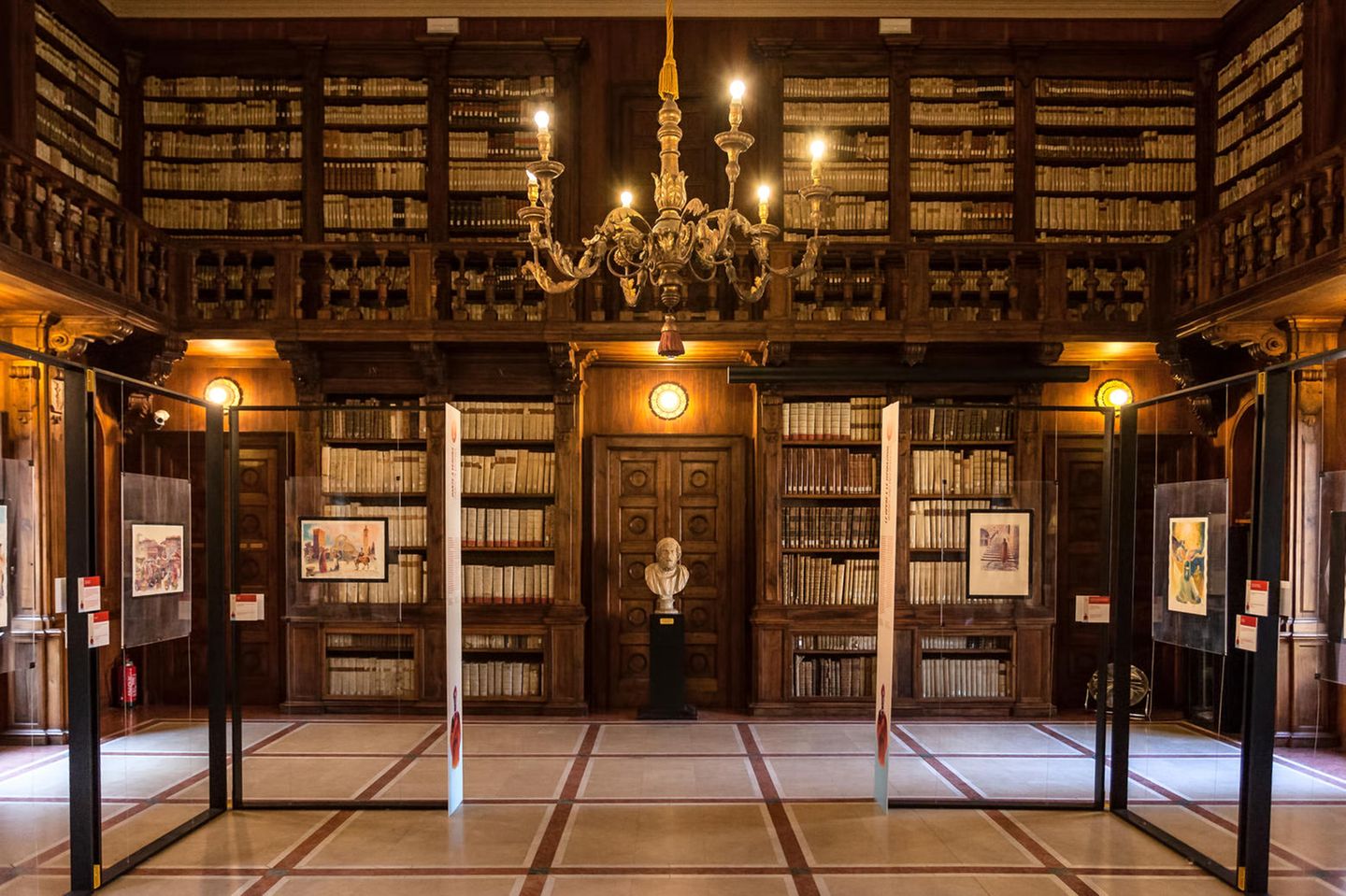 Holzregale voller Bücher über zwei Etagen mit Galerie, in der Mitte eine Büste