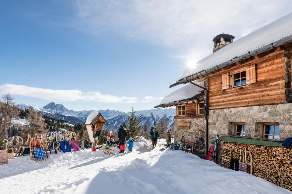 Almhütte im Schnee mit Menschen und Schlitten davor