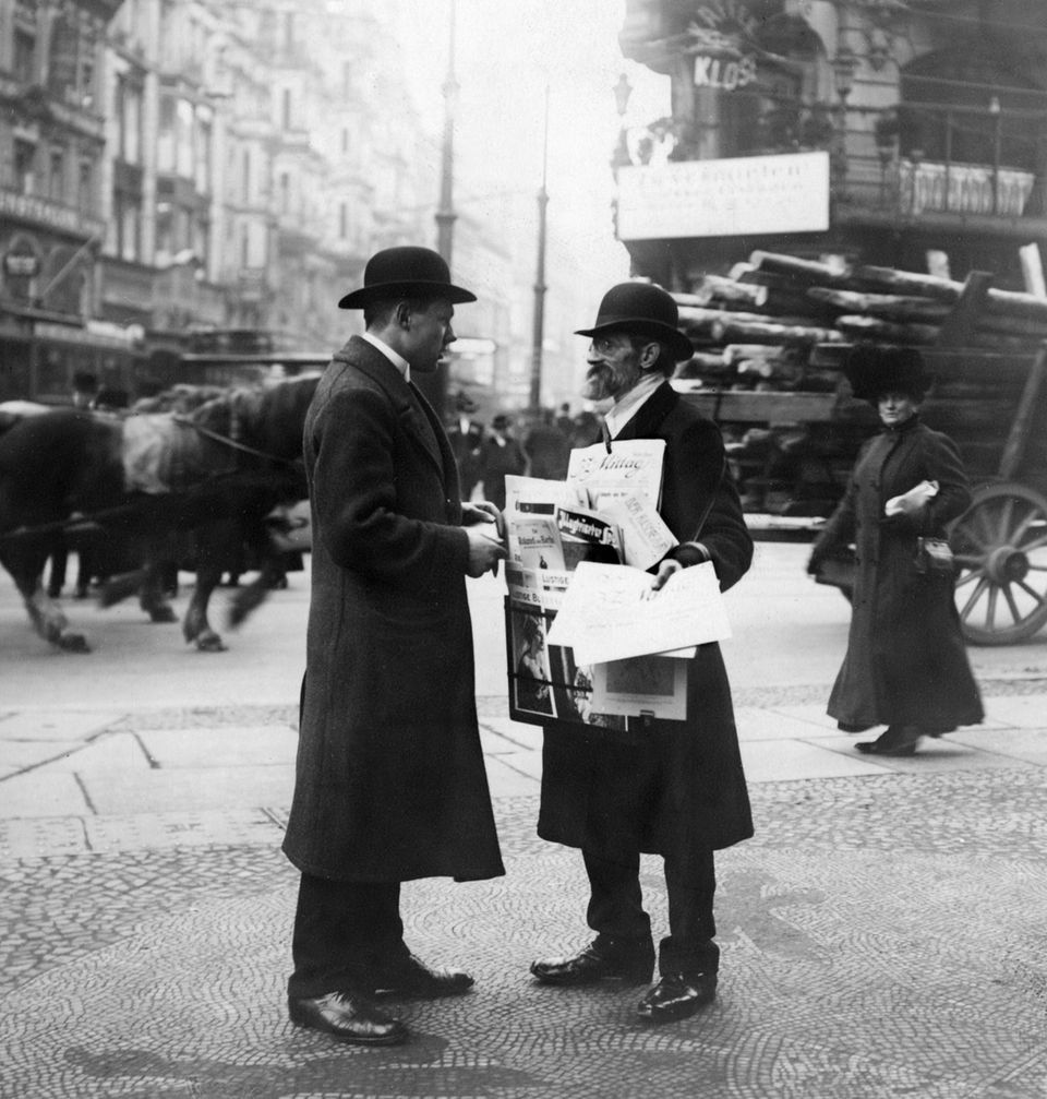 Ein Zeitungshändler mit Melone und Bart verkauft unter anderem die "B.Z. am Mittag" auf der Straße