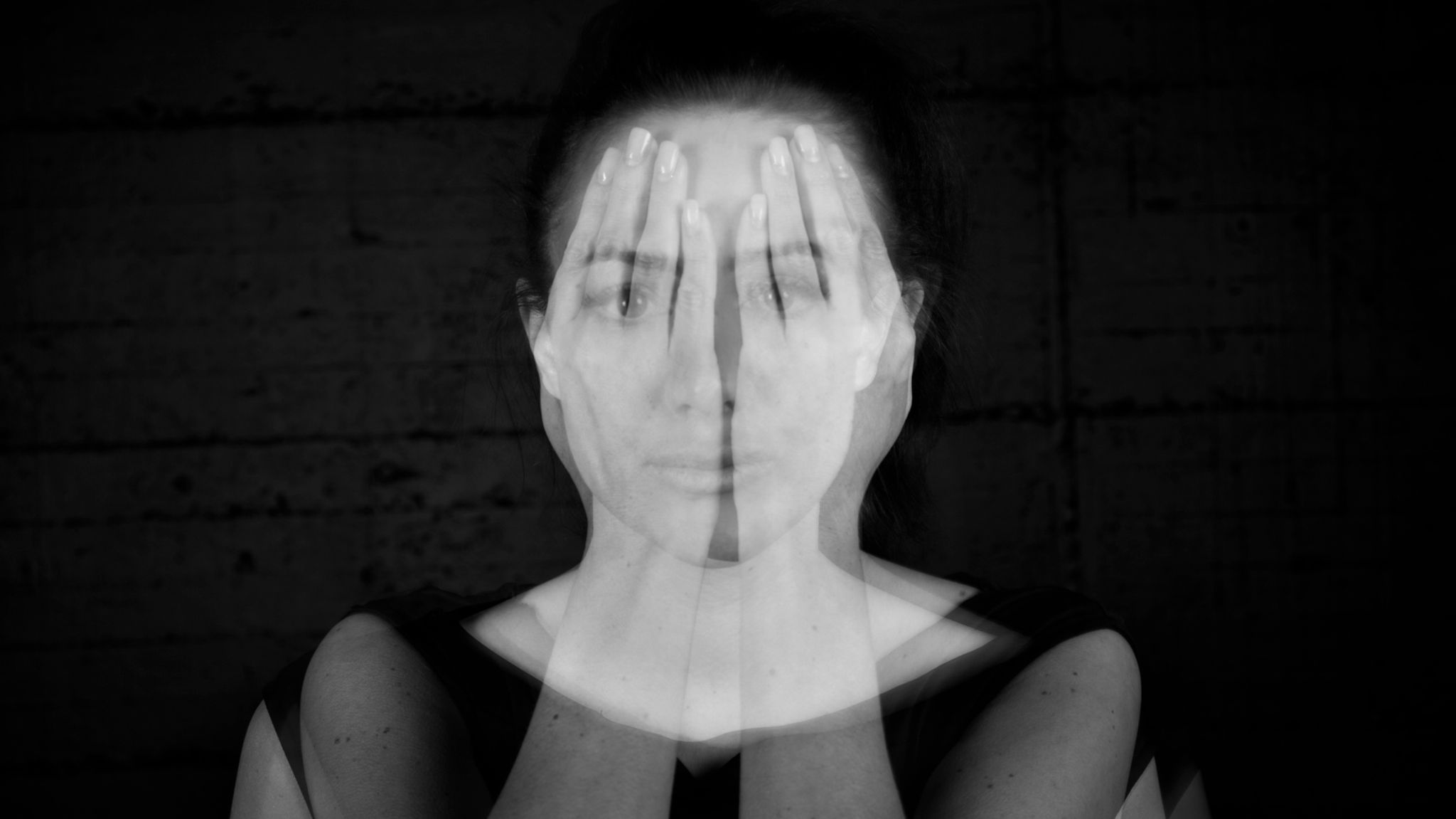 Schwarzweißfotografie, Mehrfachbelichtung: Porträt einer jungen Frau, die ihre durchscheinenden Hände vors Gesicht hält.