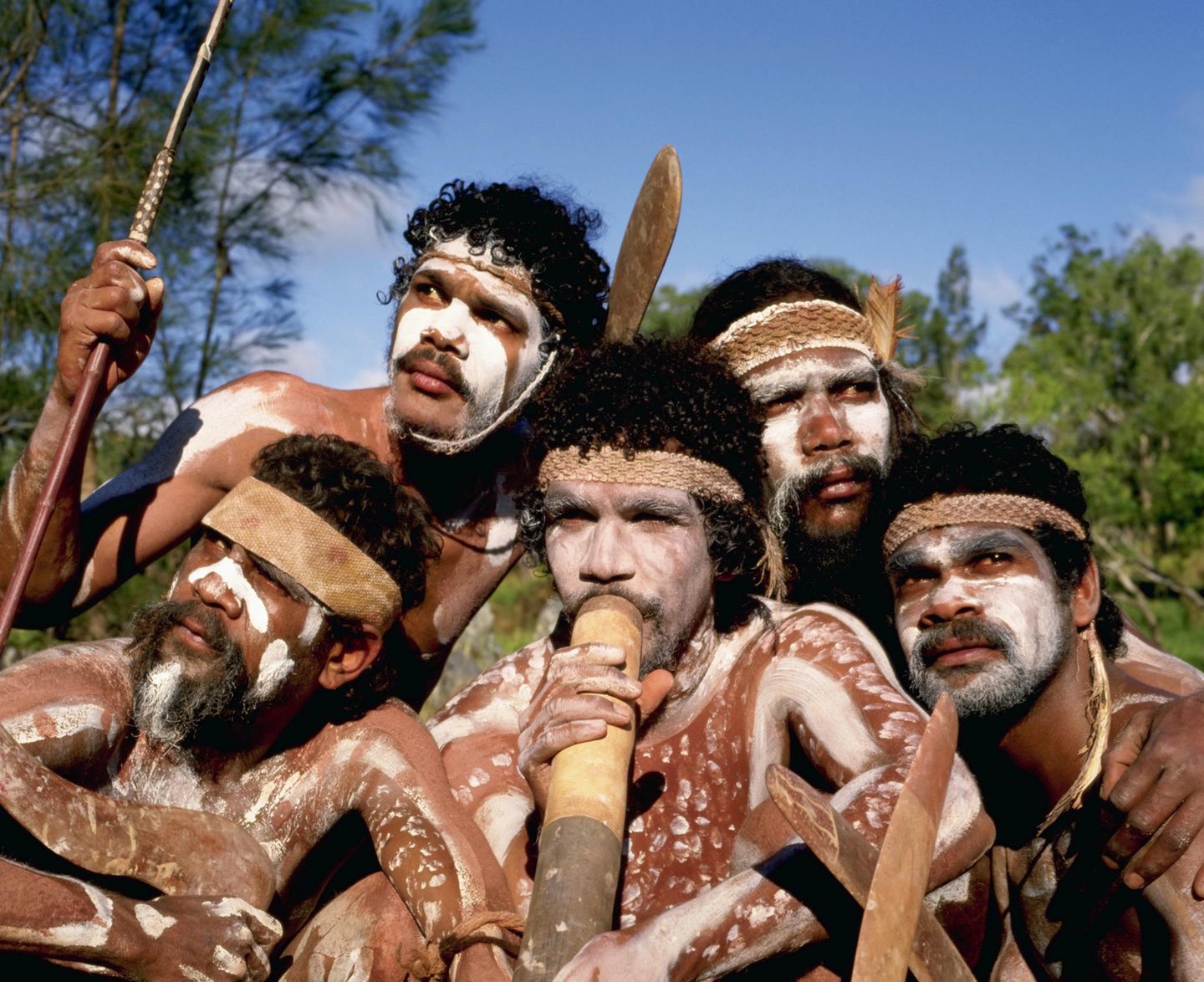Gruppe australischer Indigener mit weißer Körperbemalung, Didgeridoo und Bumerangs