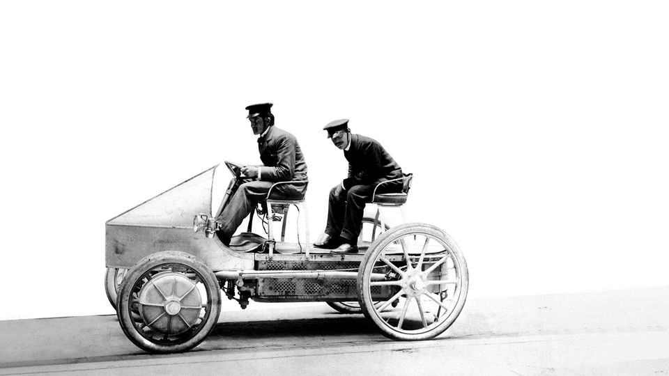 Zwei Männer mit Schirmmützen auf einem seifenkistenähnlichen Elektromobil, um 1900 Zwei Männer mit Schirmmützen auf einem seifenkistenähnlichen Elektromobil, um 1900