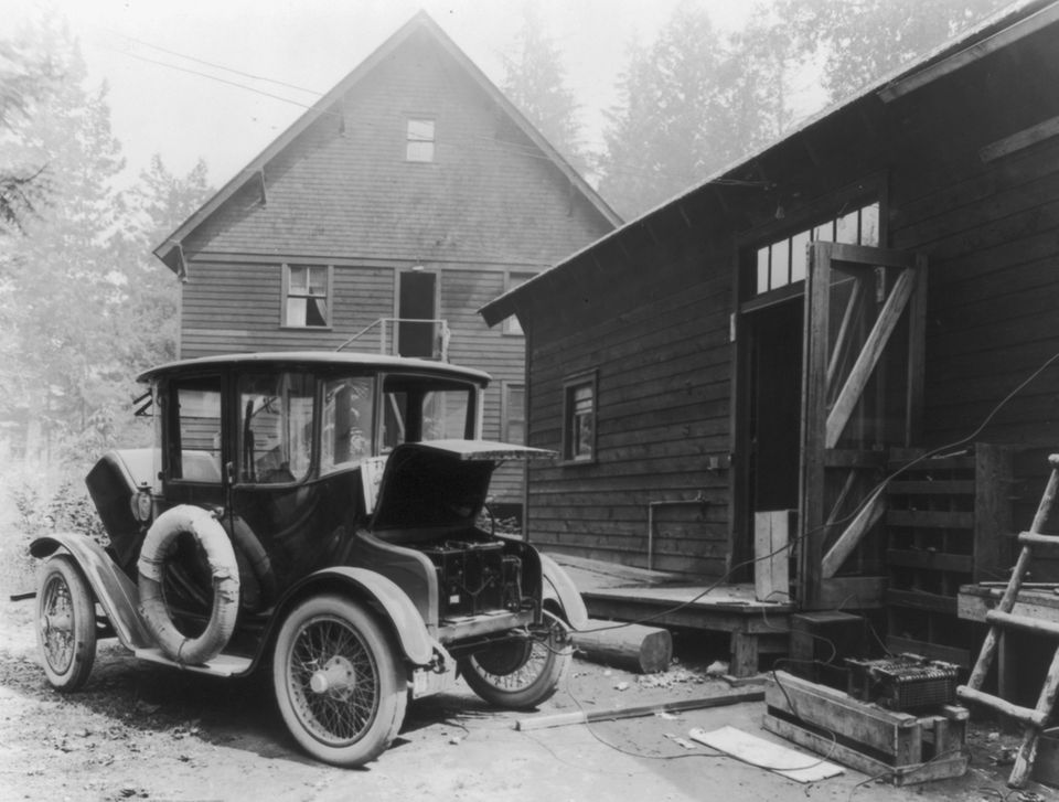 Ein frühes E-Auto mit Kabel vor einem Wohnhaus in den USA, Schwarz-Weiß-Bild um 1919 Ein frühes E-Auto mit Kabel vor einem Wohnhaus in den USA, Schwarz-Weiß-Bild um 1919