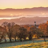 Blick über Kirche mit Zwiebelturm auf See und Berge in Dunst, Herbststimmung