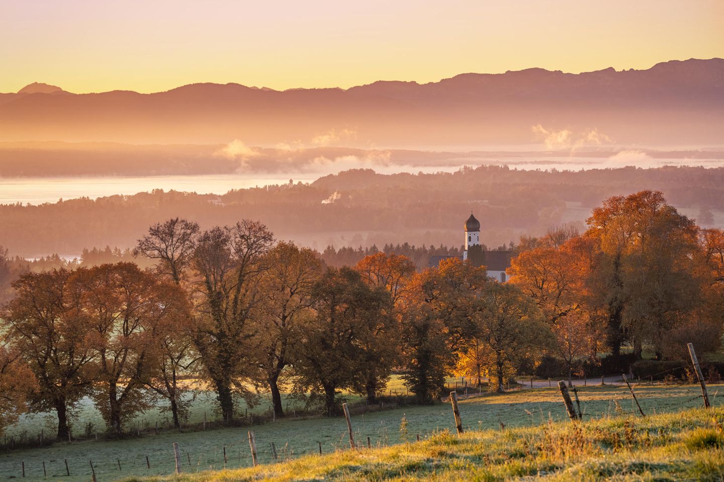Blick über Kirche mit Zwiebelturm auf See und Berge in Dunst, Herbststimmung