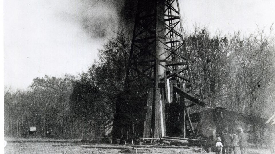 Schwarz-weiß Fotografie zeigt Rauch, der aus Ölbohrturm steigt