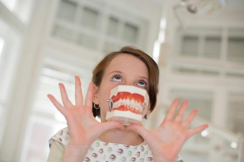 junges Mädchen hält Plastik Gebiss in die Kamera