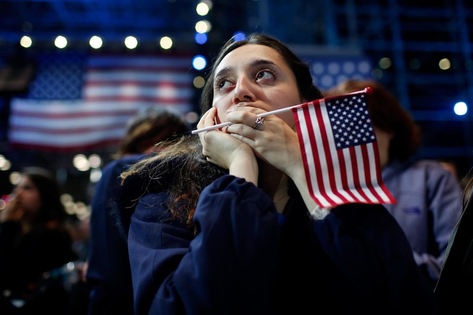 US-Wahlen: Junge Frau mit USA-Flagge in der Hand und im Hintergrund blickt nach oben 1.5004