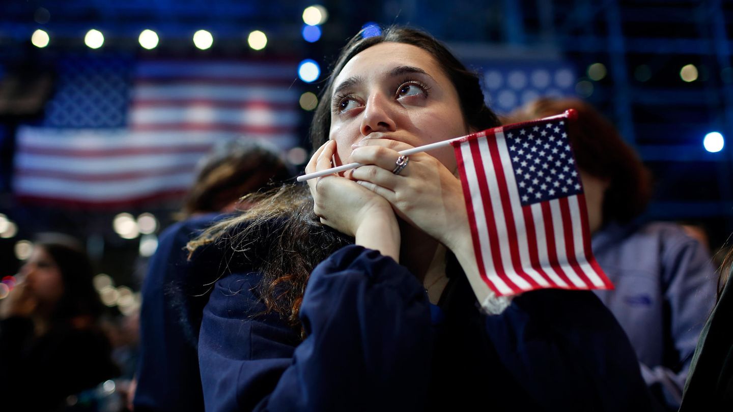 US-Wahlen: Junge Frau mit USA-Flagge in der Hand und im Hintergrund blickt nach oben