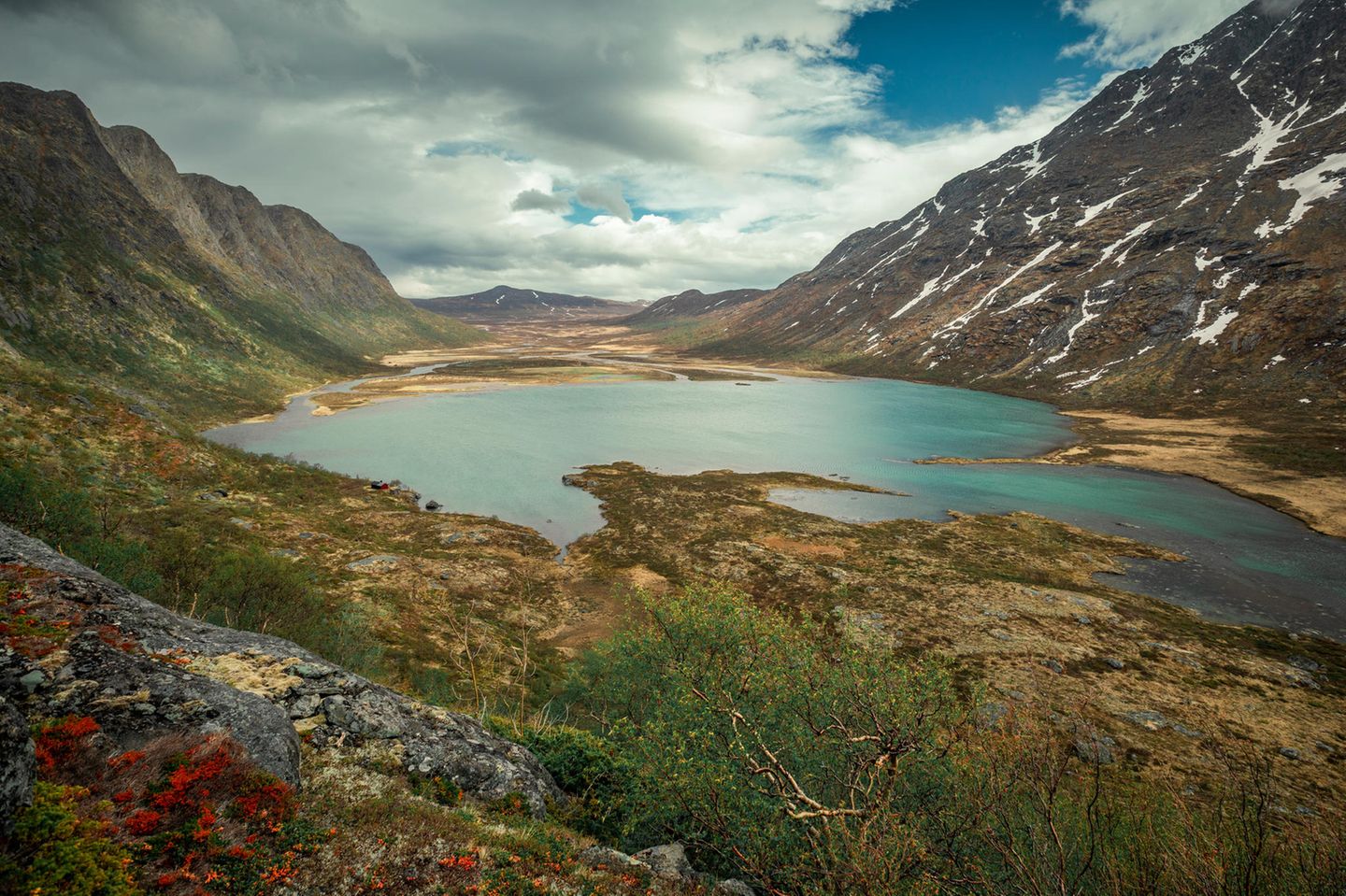 Turquoise lake surrounded by mountain landscape at Knutshoe summit in Jotunheimen National Park in Norway