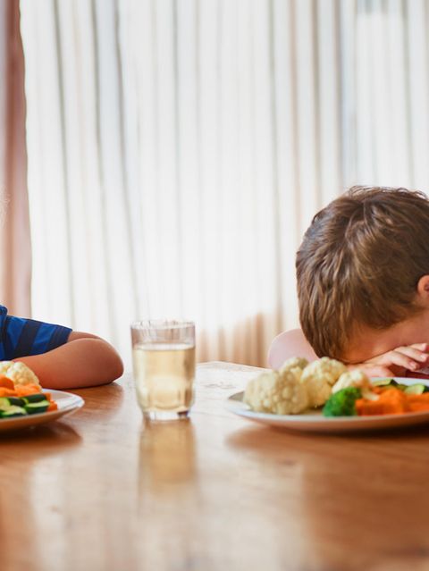 zwei verzweifelte kleine Jungs sitzen jeder vor einem Teller mit Gemüse. Einer hat den Kopf auf den Tisch gelegt
