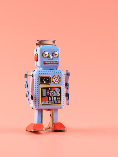 Roboter aus Blech steht vor einem lachfarbenen Hintergrund