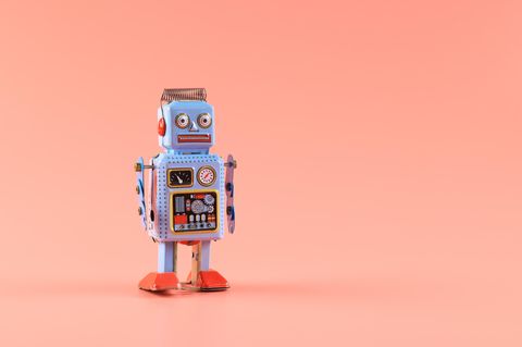 Roboter aus Blech steht vor einem lachfarbenen Hintergrund