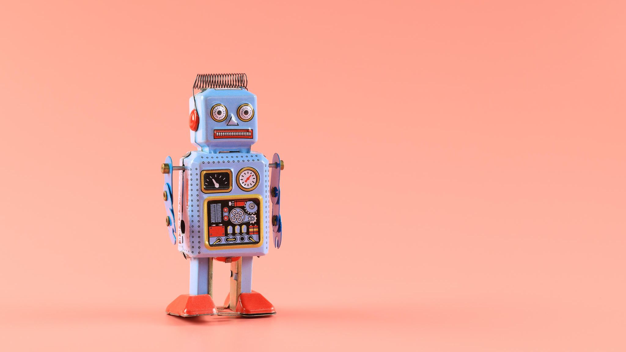 Roboter aus Blech steht vor einem lachfarbenen Hintergrund