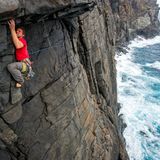 Mann klettert an Felswand über dem Meer