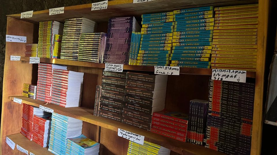 Ein stabiles Regal voller neuer Bücher, sortiert nach Klassen und Jahrgängen Menekas neue Schulbibliothek: Das Schulkomitee hat für ein Regal gesorgt, GEO schützt den Regenwald für Referenzbücher (Lehrbücher sind Aufgabe des Staates)