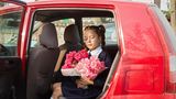 Tochter des Bürgermeisters sitzt mit Blumenstrauß in der Hand in rotem Auto