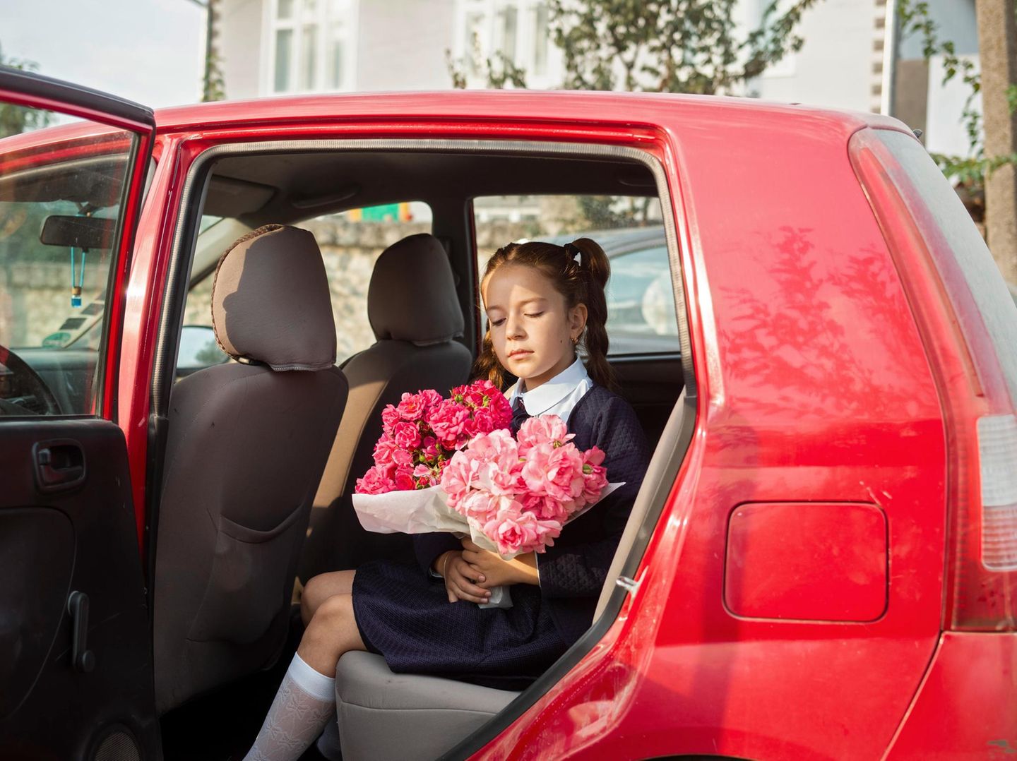 Tochter des Bürgermeisters sitzt mit Blumenstrauß in der Hand in rotem Auto