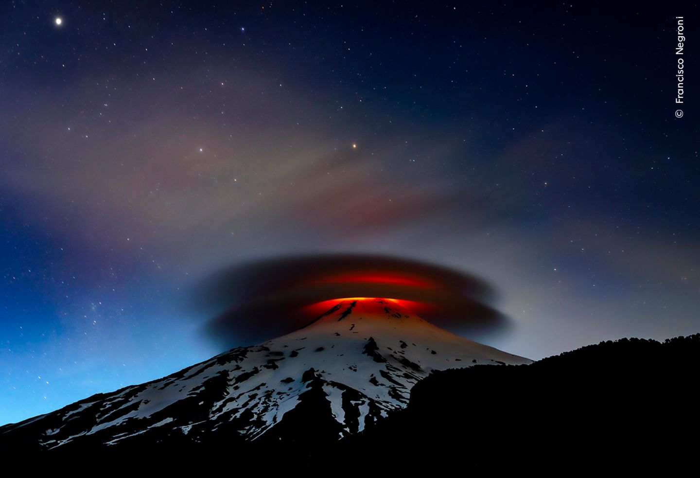 Die Lava des Vulkans Villarrica beleuchtet eine kreisförmige, zweischichtige Wolke die, die Spitze  Vulkans umhüllt.