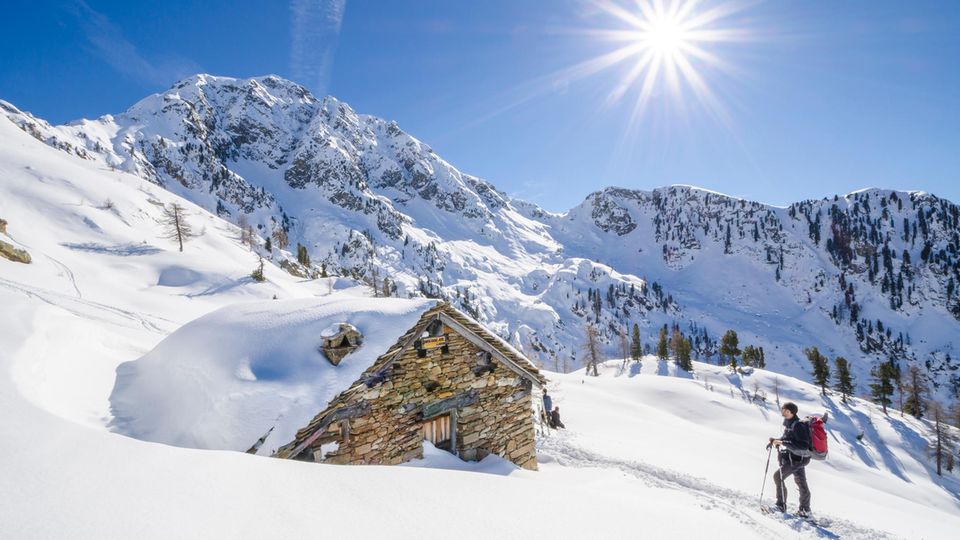 Mensch in verschneiter Landschaft mit Skiern vor Hütte Mensch in verschneiter Landschaft mit Skiern vor Hütte