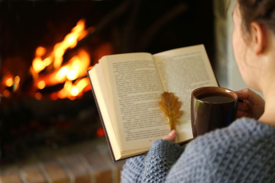 Frau sitzt an Kamin mit Buch in de rHand 1.5004