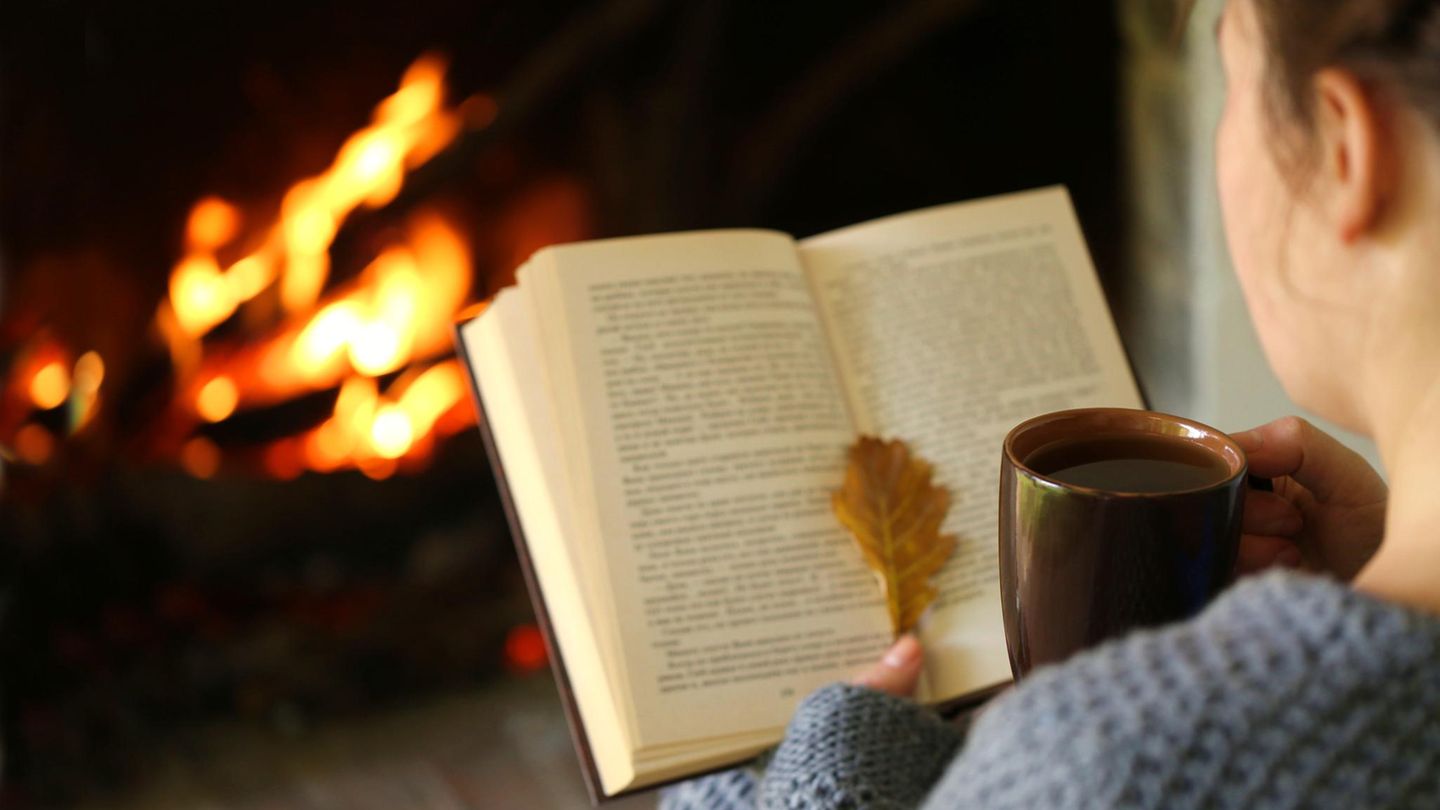 Frau sitzt an Kamin mit Buch in de rHand