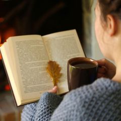 Frau sitzt an Kamin mit Buch in de rHand
