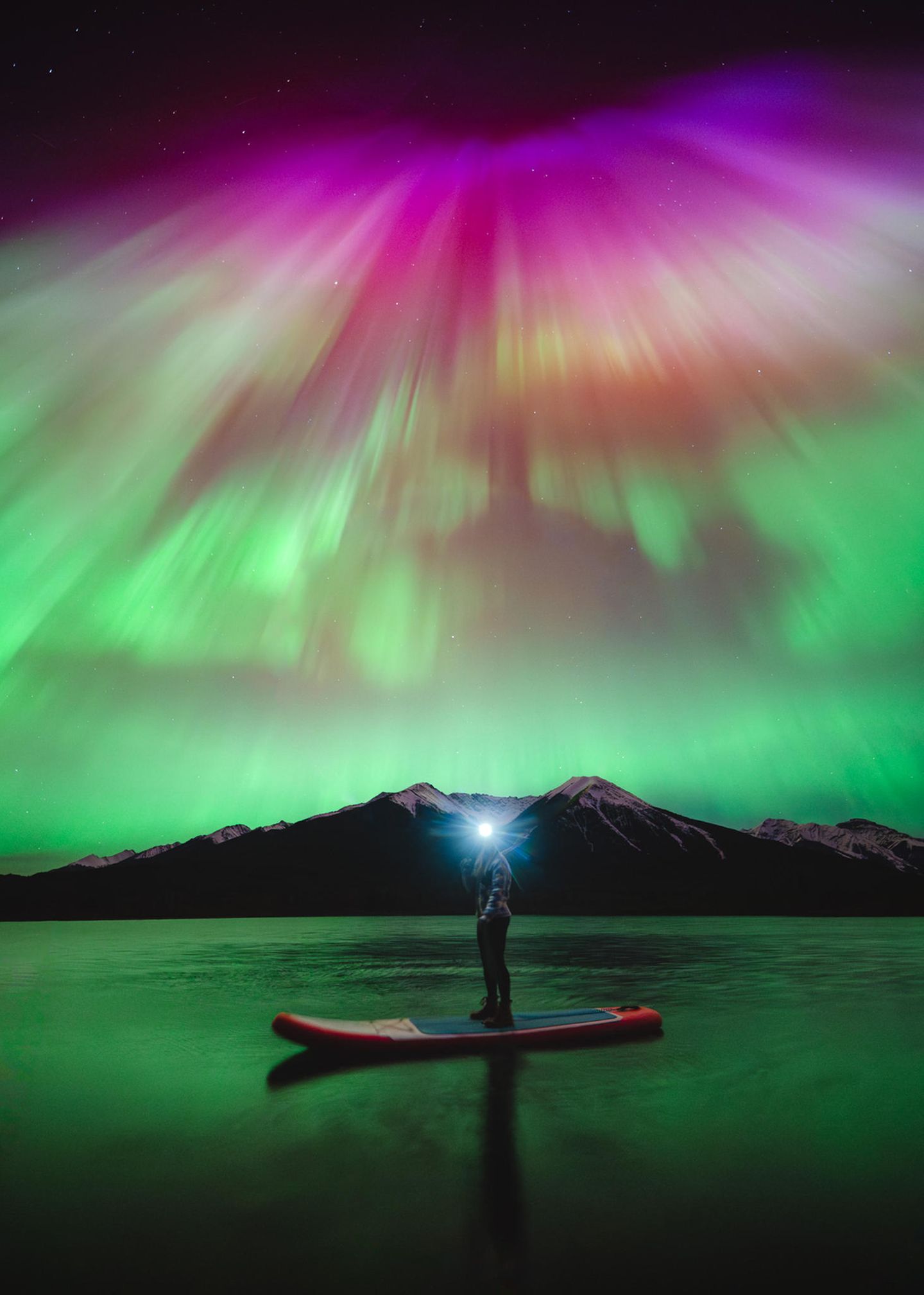 Im kanadischen Banff-Nationalpark fotografierte Herry Himanshu eine Freundin mit Stirnlampe unter einem in Rot-, Rosa- und Violetttönen flirrenden Nachthimmel.