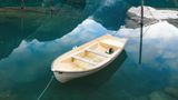 Im Vordergrund ein Boot im türkisfarbenen Wasser. Im Hintergrund eine Bergkette