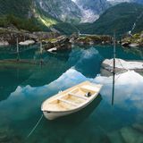 Im Vordergrund ein Boot im türkisfarbenen Wasser. Im Hintergrund eine Bergkette