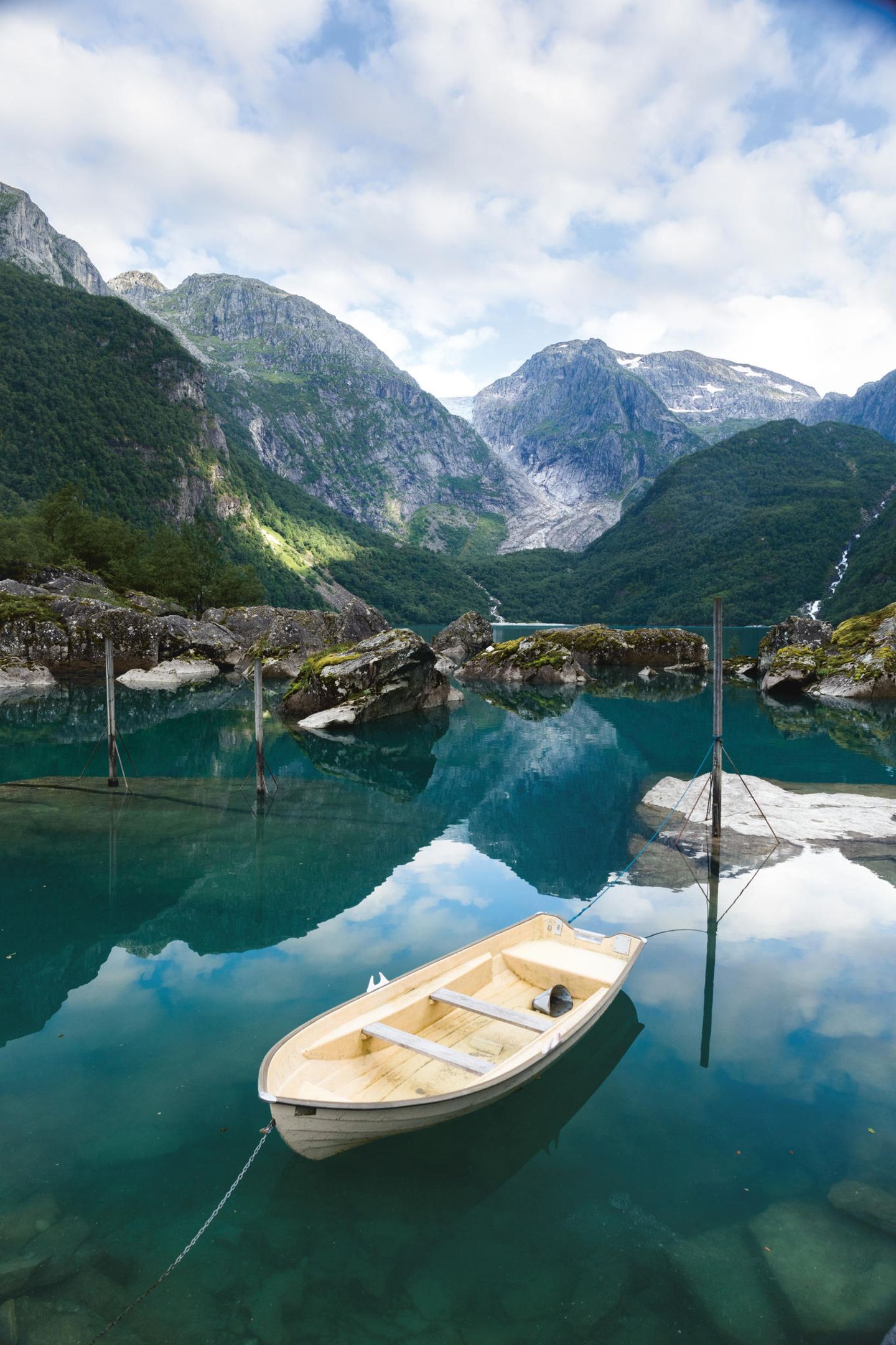 Im Vordergrund ein Boot im türkisfarbenen Wasser. Im Hintergrund eine Bergkette